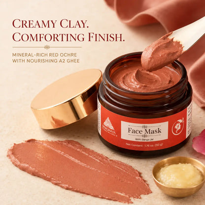 An open amber jar of face mask with a gold lid beside it, a spoonful of creamy clay-colored mask above, a smear of the mask below, and a small gold bowl of ghee on a beige surface. Text reads: 'Creamy Clay.
