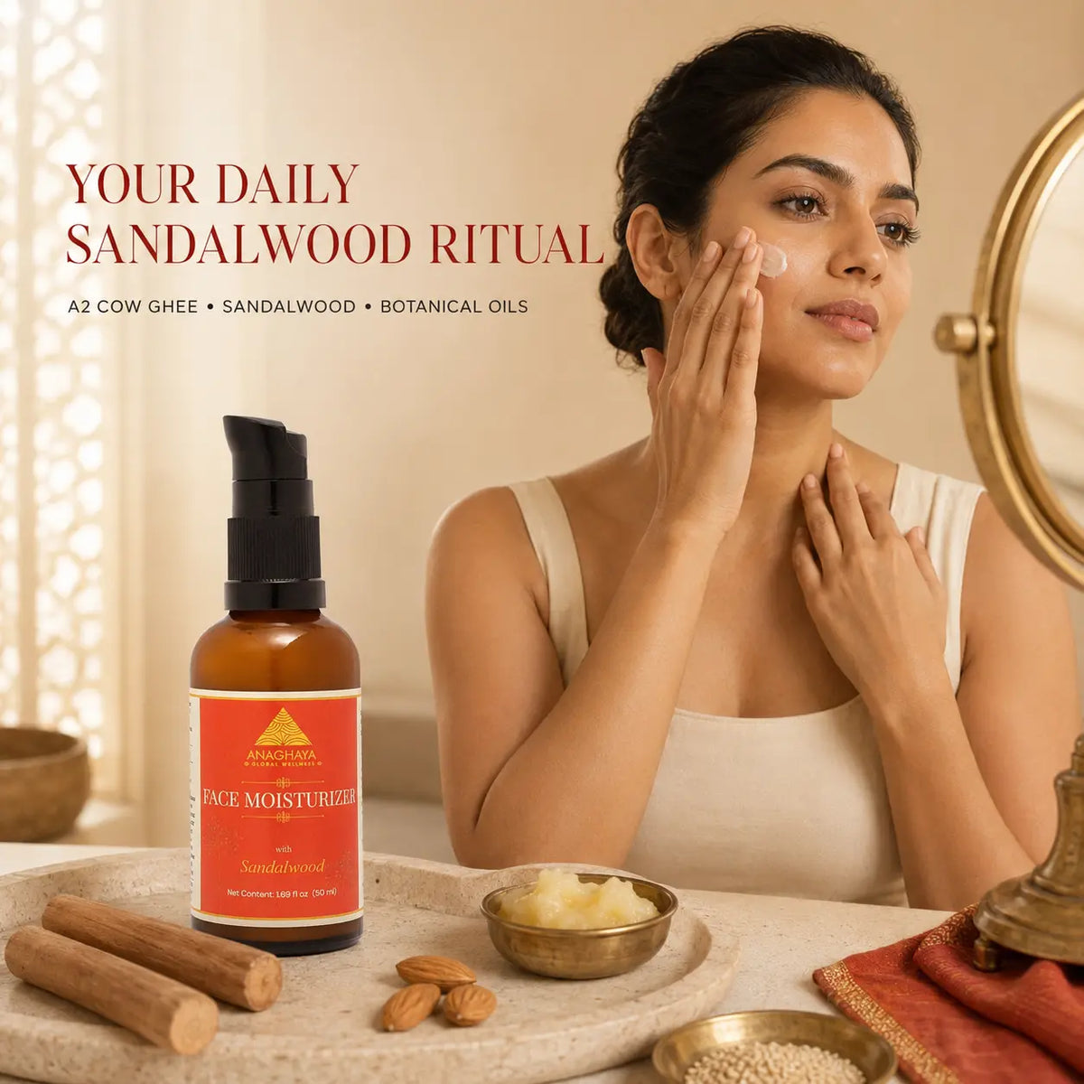 A woman applies cream to her face while looking into a mirror in a warm, spa-like setting. A bottle of Sandalwood Face Moisturizer by A2 Cow Ghee is displayed in the foreground with cinnamon sticks, bowls, and text reading 'YOUR DAILY SANDALWOOD RITUAL'.